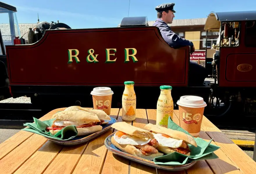 The Pullman First Class Breakfast Experience at the Ravenglass and Eskdale Railway with a steam train in the background.